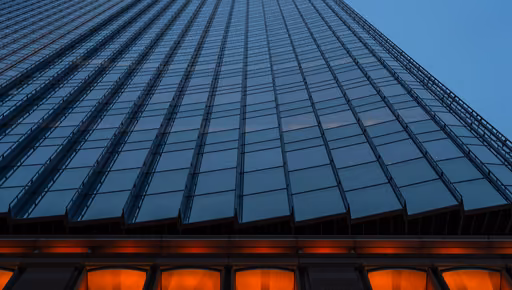 Glass curtain wall of an office tower at blue hour, its lit base glowing below