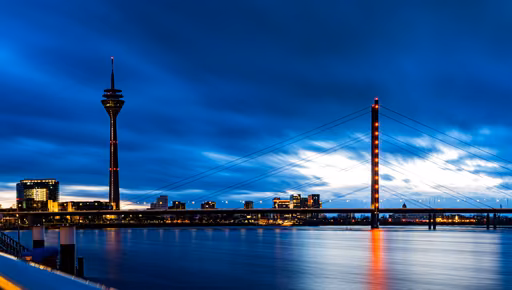 A riverside tower and a cable bridge under fast-moving evening clouds