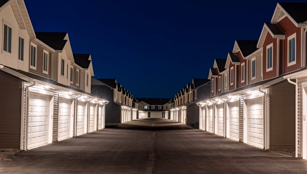 A row of townhouses with lit garage doors under a deep blue sky