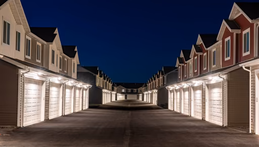 A row of townhouses with lit garage doors under a deep blue sky