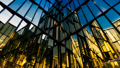 Glass facade seen from below at blue hour, the lit interior showing through