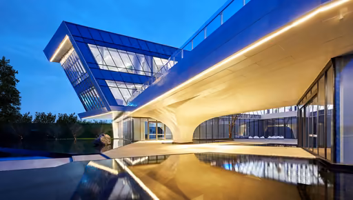 A glass building resting on a lit, sculpted base at blue hour